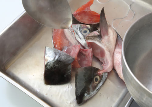 鮭のアラ全体に熱湯をかけて霜降りにし、手で鱗や汚れを取り除く。お湯を切り、水分を取っておく。
