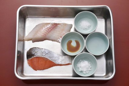 左下は生鮭（切り身１枚・約100ｇ）、左上は生鱈（切り身１枚・約100ｇ）、右の器は切り身１枚分の調味料で、手前から砂糖10ｇ、醤油少々、酒小さじ２、塩２ｇ。生鮭、生鱈とも調味料は同量。