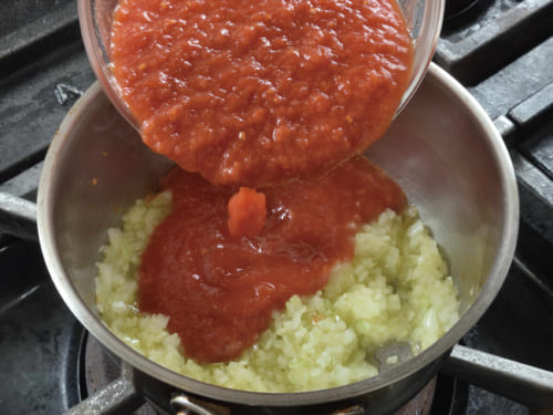 トマトの水煮をつぶして入れ、中火で約４分、弱火でさらに約１分煮て、塩をひとつまみ入れ火を止める。