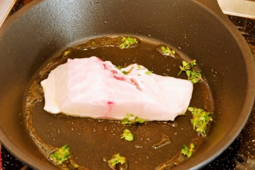 フライパンにオリーブオイルをハーブとともに熱し、水気を拭き取った鯛を皮目からやや強火で焼く